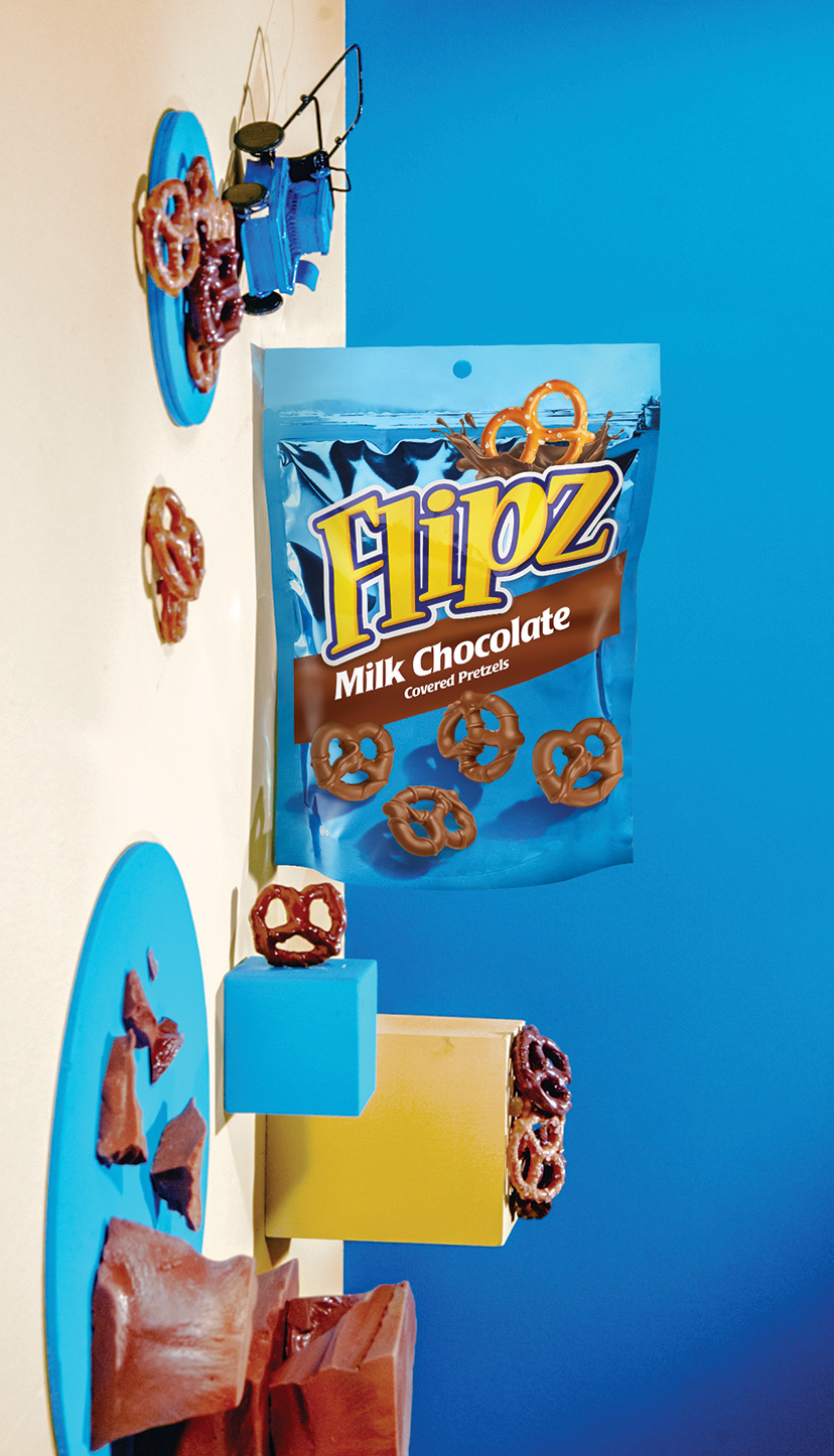 Blue bag of milk chocolate covered pretzels with pieces of chocolate laying about